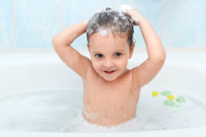 Little Cute Girl Taking Bath, Washing Her Hair With Shampoo By Herself, Looks Happy Playing With Foam Bubbles, Looking Directly At Camera, Infant Enjoys Being In Warm Water, Charming Baby Taking Bath.