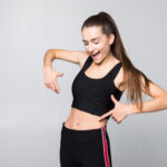 Fitness, Exercise And Diet Concept. Portrait Of Woman Pointing Finger At Her Six Pack Isolated On White Background