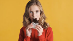 Beautiful Teenager Girl Eating Chocolate Bar Isolated On Yellow
