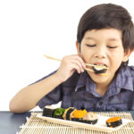 Asian lovely boy is eating sushi isolated over white background