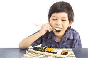 Asian Lovely Boy Is Eating Sushi Isolated Over White Background